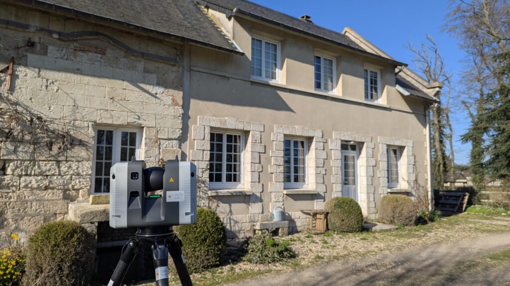 Scanner laser au premier plan devant une maison en pierre